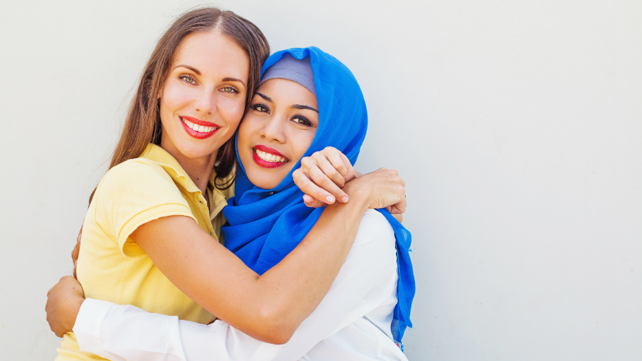 Two women hugging each other. One of them is wearing a headscarf.
